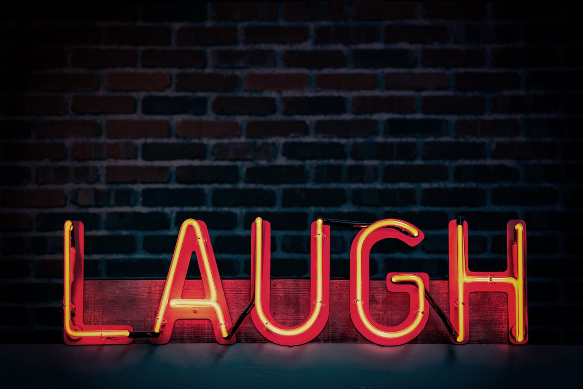 Leuchtende „Laugh“-Schrift vor einer Backsteinwand in einem Comedy-Club.